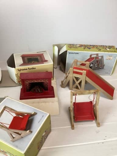 Une cheminée rouge, un toboggan et une balançoire en bois miniatures, posés devant leurs boîtes Sylvanian Families.